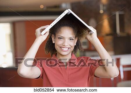 Picture - African woman holding laptop on head. Fotosearch