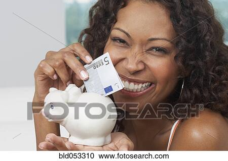 Stock Image - African woman putting money in piggyback. Fotosearch
