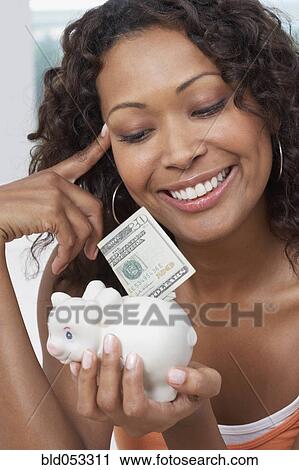 Stock Image - African woman putting money in piggyback. Fotosearch