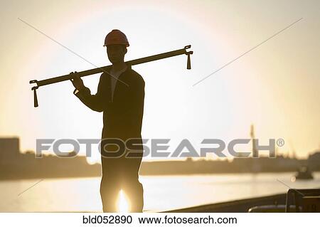 Stock Image - Asian male dock worker holding pipe. Fotosearch