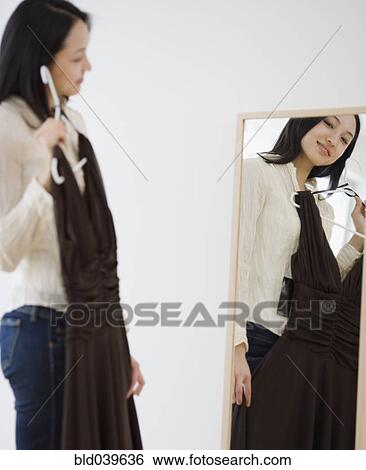 Asian woman holding dress up in front of mirror View Large Photo Image Stock Photograph - Asian woman holding dress up in front of mirror. Fotosearch