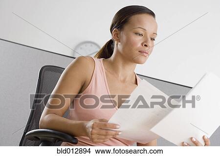 Picture - Businesswoman reading papers in office. Fotosearch