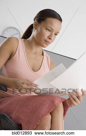 Stock Image - Businesswoman reading papers in office. Fotosearch