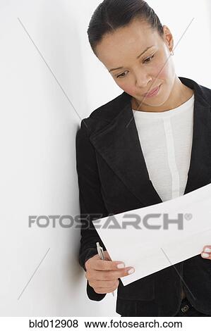 Stock Photo - Businesswoman reading paperwork while leaning against wall. Fotosearch