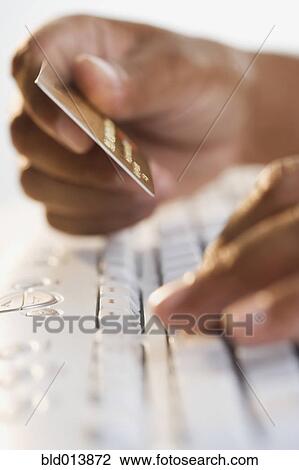 Stock Image - Close up of hands typing on keyboard and holding credit card . Fotosearch