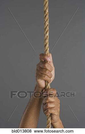 Stock Photo - Close up of two hands hanging on rope. Fotosearch