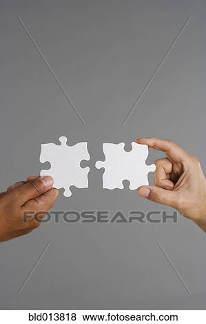 Stock Photo - Close up of two hands holding puzzle pieces. Fotosearch