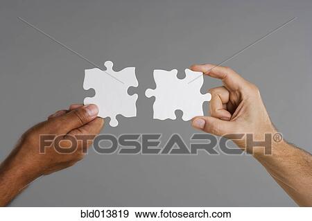 Stock Photo - Close up of two hands holding puzzle pieces. Fotosearch