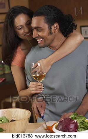 Stock Photo - Couple hugging and drinking while cooking. Fotosearch