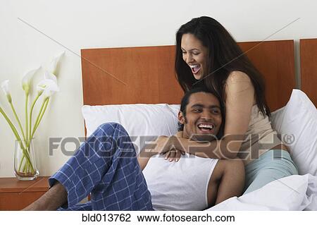 Stock Image - Couple hugging and laughing in bed. Fotosearch