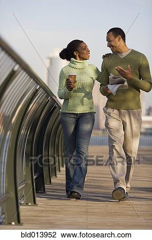 Stock Image - Couple walking across bridge with city behind them. Fotosearch