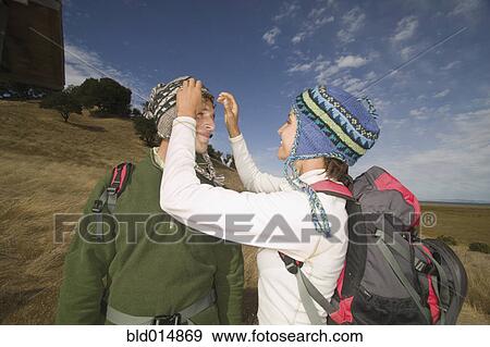 Stock Photo - Couple wearing backpacks and adjusting caps. Fotosearch