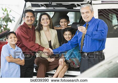 Stock Image - Hispanic car salesman handing car keys to family. Fotosearch
