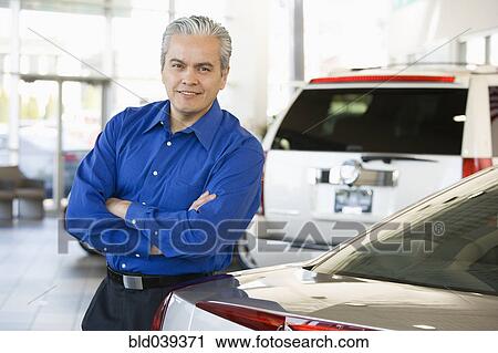 Stock Image - Hispanic car salesman leaning on new car. Fotosearch