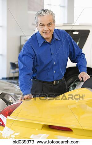Stock Image - Hispanic car salesman looking at new car. Fotosearch