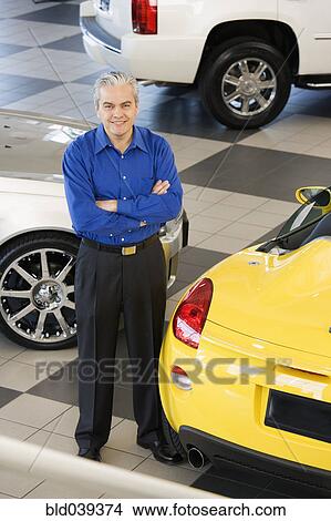 Picture - Hispanic car salesman next to new cars. Fotosearch