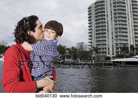 Stock Image - Hispanic father and son hugging outdoors. Fotosearch