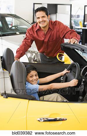 Stock Image - Hispanic father and son looking at new car. Fotosearch