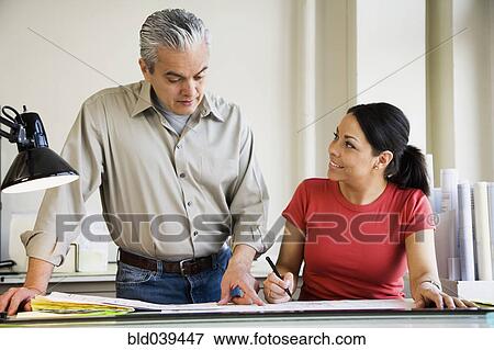 Stock Photo - Hispanic male and female architects looking at blueprints. Fotosearch