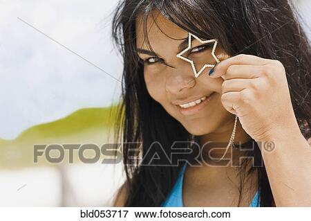 Stock Photo - Hispanic woman holding heart necklace over eye. Fotosearch