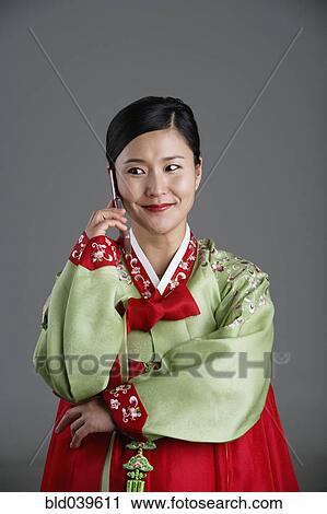 Stock Image - Korean woman in traditional dress talking on cell phone. Fotosearch