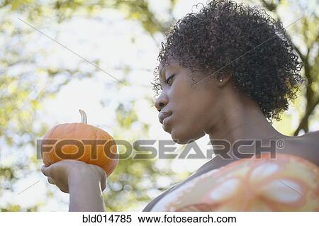 Stock Photography - Low angle portrait of woman holding pumpkin. Fotosearch