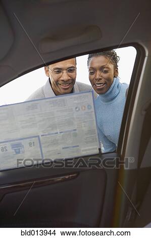 Low angle view of couple looking at sticker on new car window View Large Photo Image Picture - Low angle view of couple looking at sticker on new car window. Fotosearch