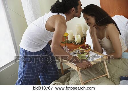 Stock Photo - Man kissing woman as he serves her breakfast in bed. Fotosearch