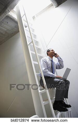 Man on ladder with laptop and mobile phone View Large Photo Image Picture - Man on ladder with laptop and mobile phone. Fotosearch