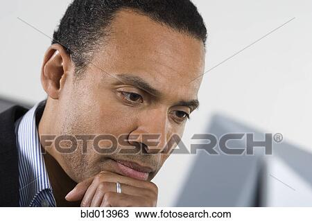 Man thinking with hand on chin while looking at computer View Large Photo Image Stock Image - Man thinking with hand on chin while looking at computer. Fotosearch