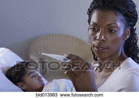 Stock Image - Mother reading thermometer reading with sick daughter. Fotosearch