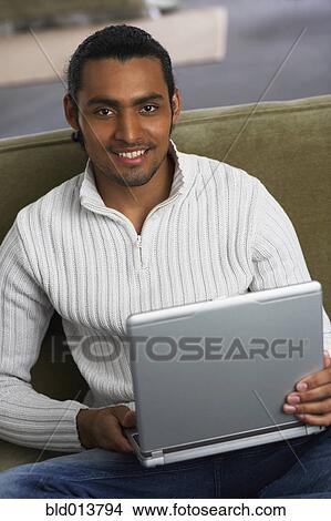 Picture - Portrait of man on couch with laptop. Fotosearch