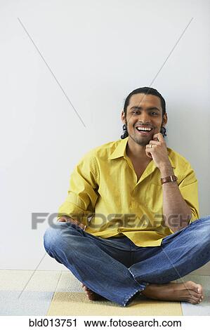 Stock Image - Portrait of man sitting cross legged on floor laughing. Fotosearch