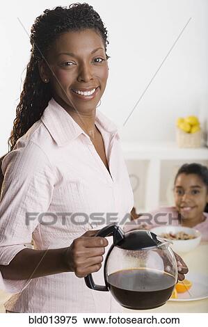 Stock Photography - Portrait of mother holding coffee pot and daughter at table. Fotosearch