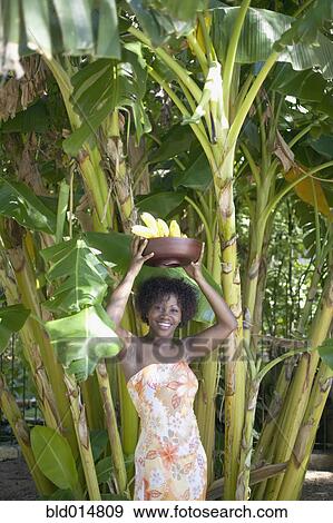 Stock Photo - Portrait of woman in grove of trees with bananas over head. Fotosearch
