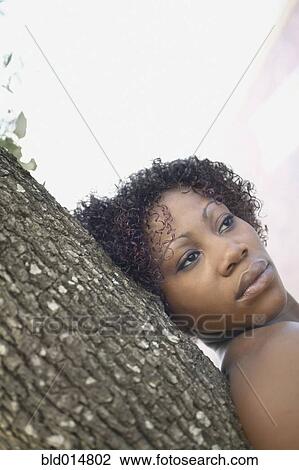 Stock Image - Portrait of woman leaning against tree. Fotosearch
