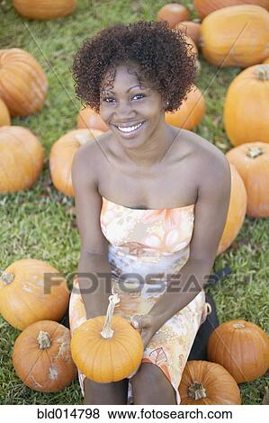 Stock Photo - Portrait of woman sitting in pumpkin field. Fotosearch