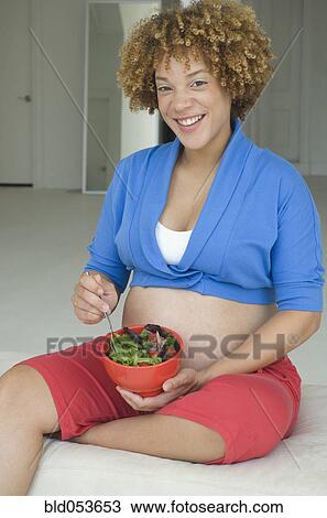 Stock Image - Pregnant African woman eating salad. Fotosearch