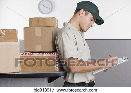 Profile of delivery man writing in clipboard with stack of boxes behind him View Large Photo Image Stock Photo - Profile of delivery man writing in clipboard with stack of boxes behind him. Fotosearch