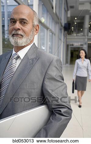Stock Image - Senior African businessman carrying laptop. Fotosearch
