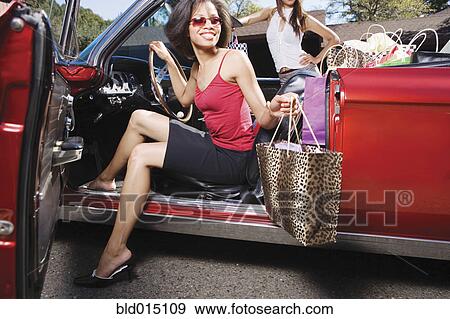 Stock Photo - Two women getting out of convertible after shopping. Fotosearch