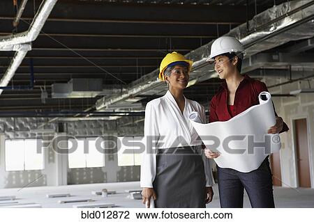 Stock Image - Two women in hard hats at construction site. Fotosearch