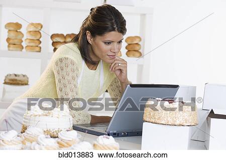 Stock Image - Woman at bakery working on laptop. Fotosearch