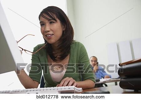 Woman at desk with man in background View Large Photo Image Stock Photo - Woman at desk with man in background. Fotosearch