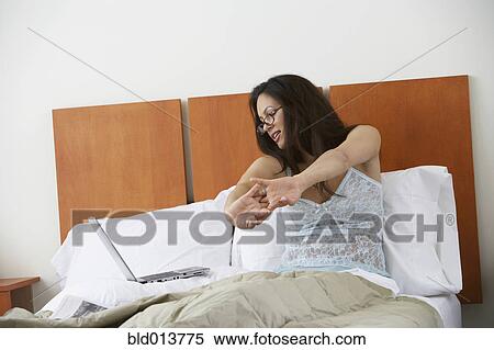 Stock Photography - Woman in bed stretching while looking at laptop. Fotosearch