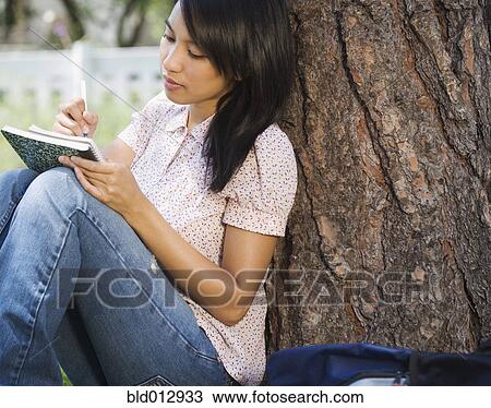 Woman sitting against tree writing in notebook View Large Photo Image Stock Image - Woman sitting against tree writing in notebook. Fotosearch