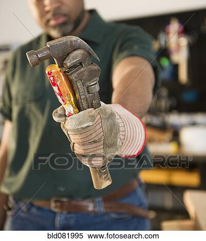 Stock Photography - African American carpenter holding screwdriver, wrench and hammer. Fotosearch