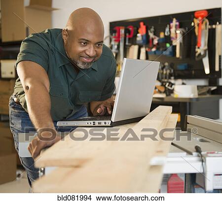 Picture - African American carpenter using laptop in workshop. Fotosearch