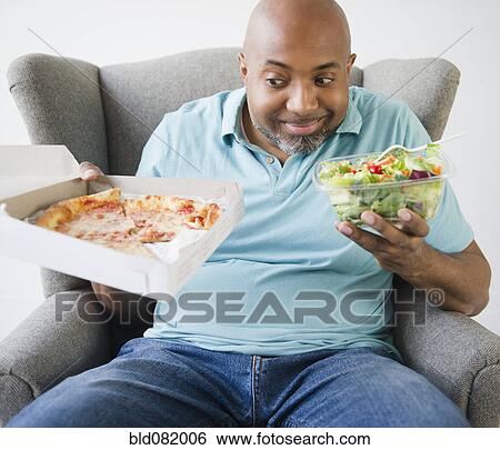 Stock Photograph - African American deciding between salad and pizza. Fotosearch