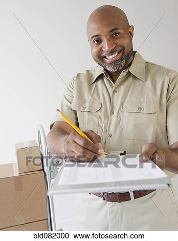 Stock Image - African American deliveryman holding out clipboard for signature. Fotosearch